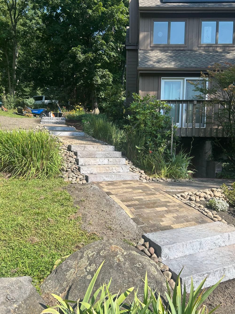 Stone pathway leading to a house, surrounded by greenery and landscaping features.