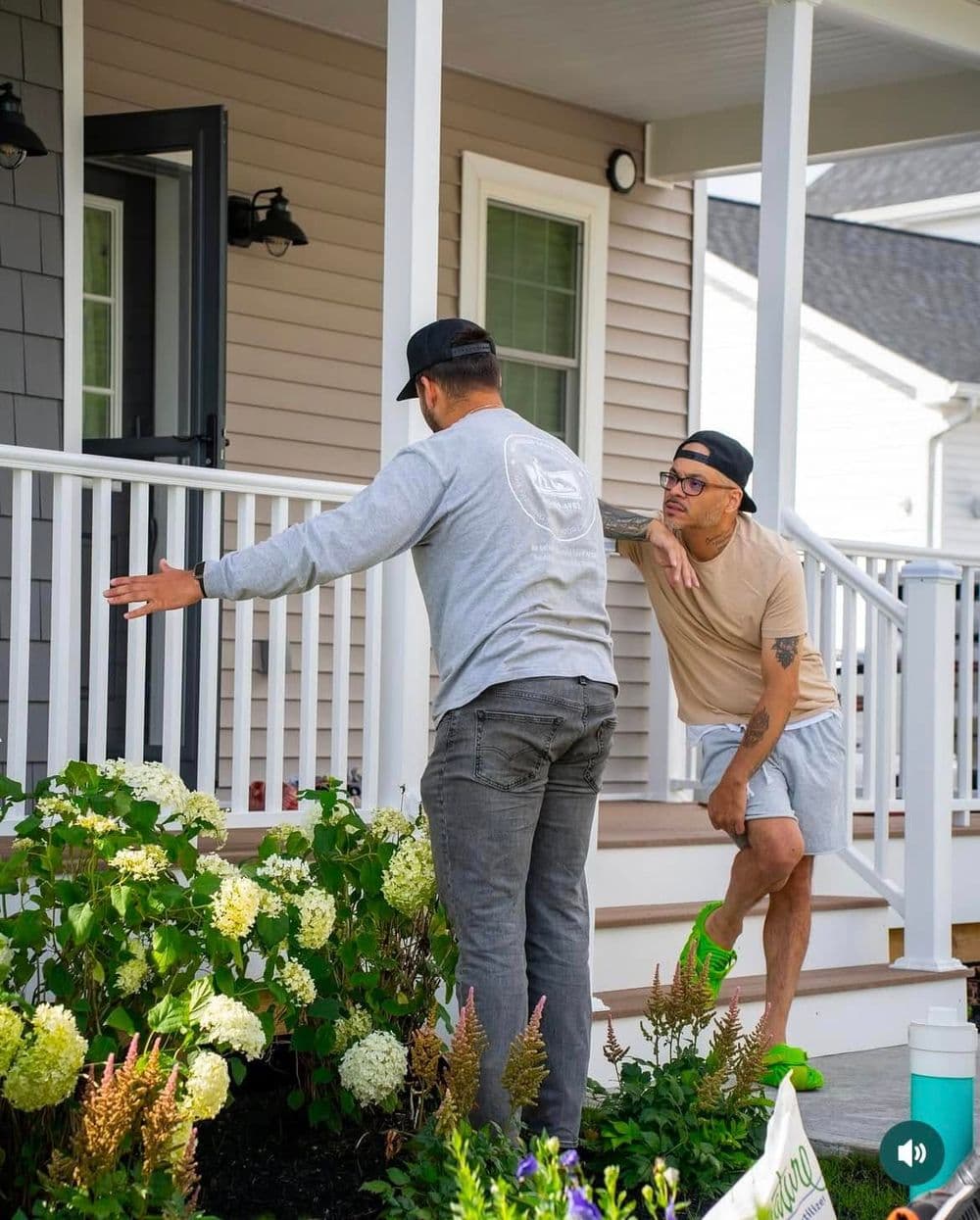 Two men discussing landscaping in front of a house with blooming hydrangeas in daylight.
