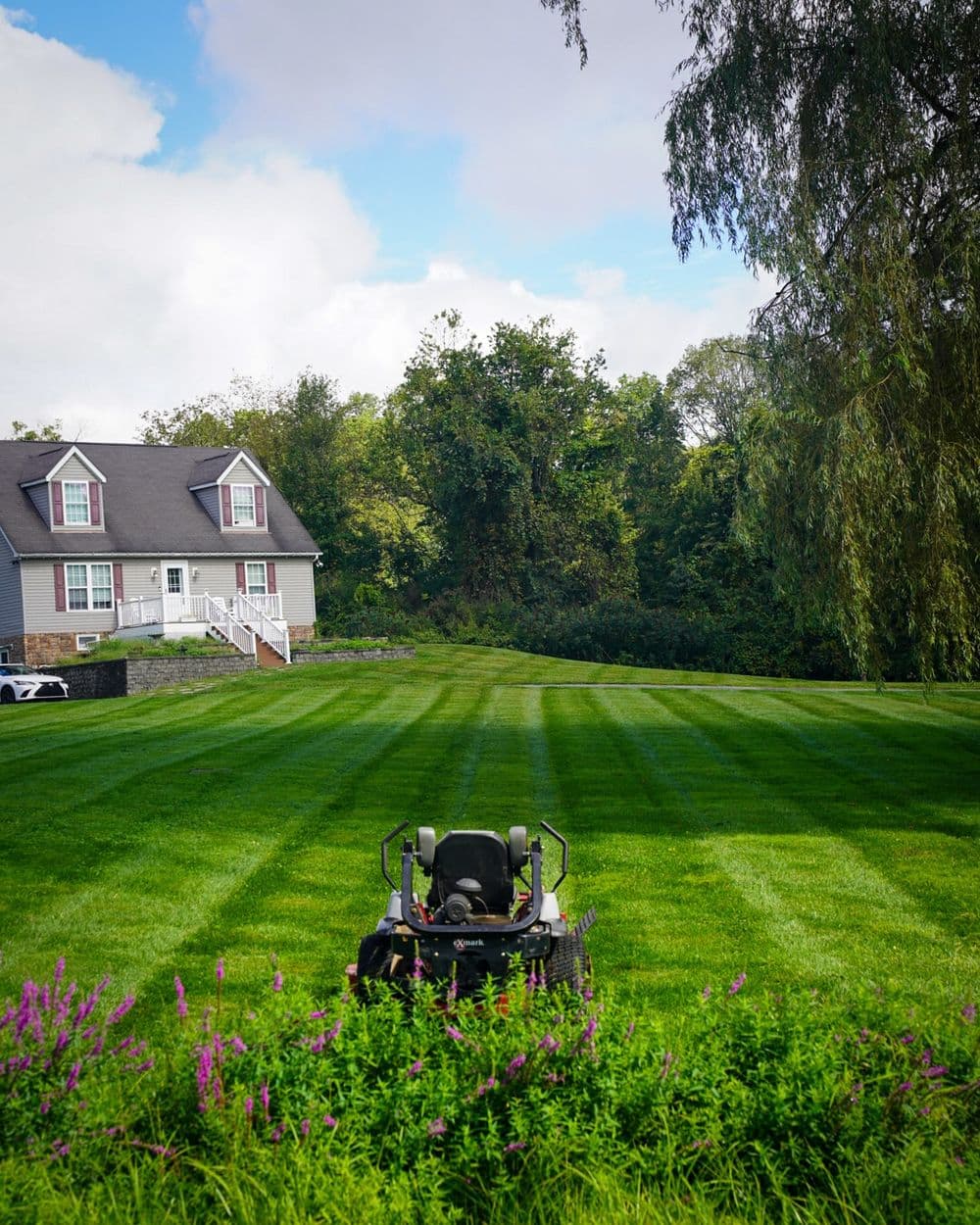 Lawn mower positioned in a lush green yard with a house and trees in the background.
