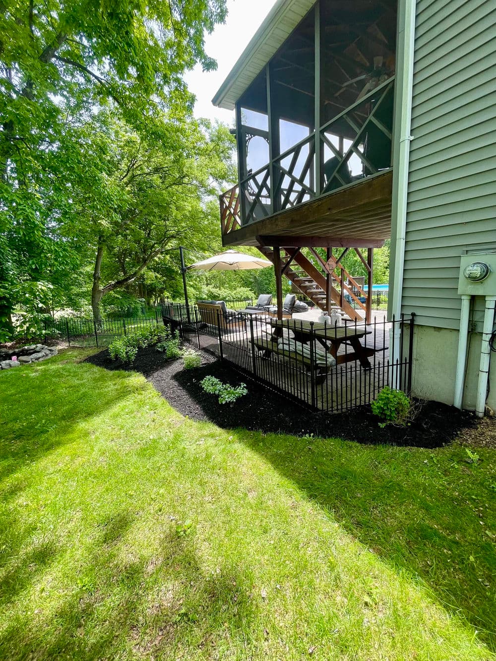 Backyard patio with seating under a screened porch, lush greenery, and landscaped garden.